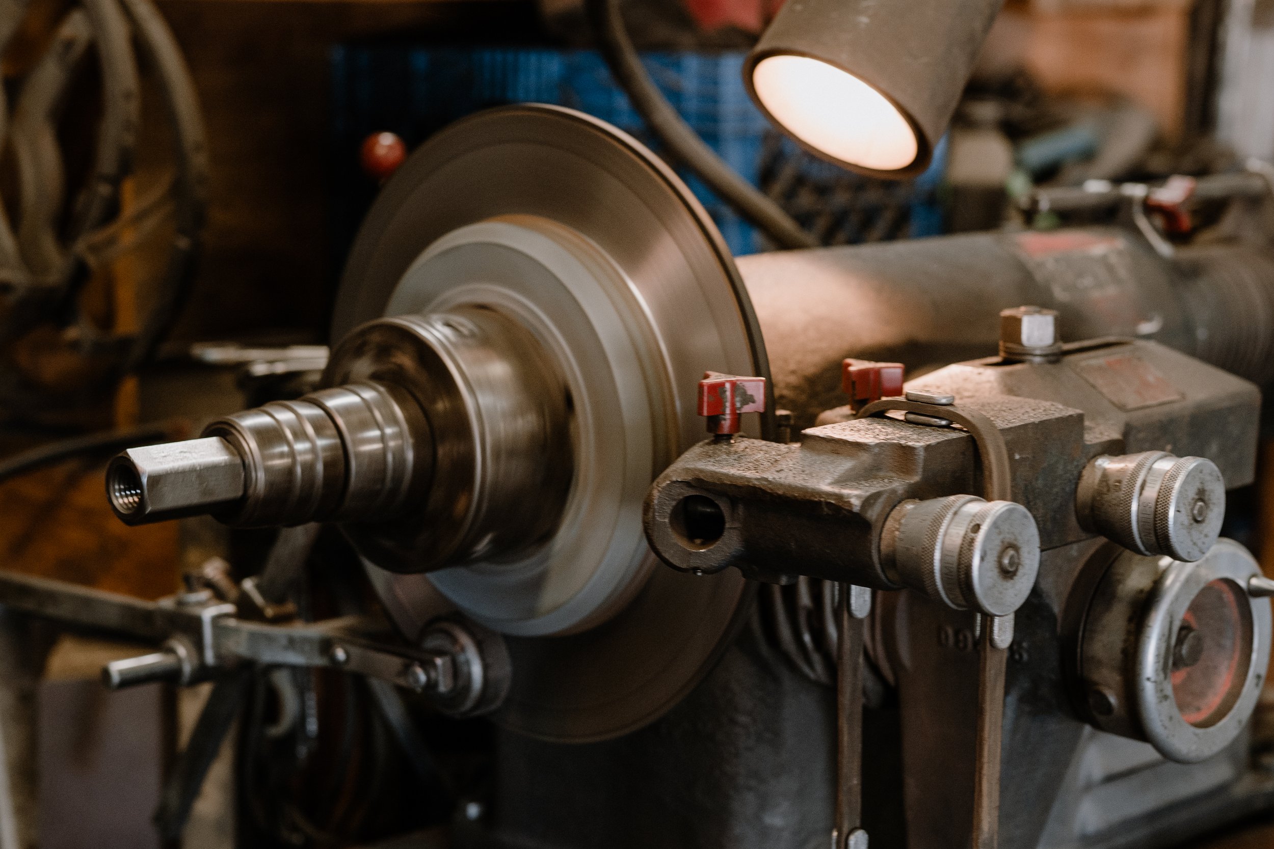 A close-up view of a metal lathe machine in a workshop, with a rotating metal workpiece being machined and illuminated by a focused light.