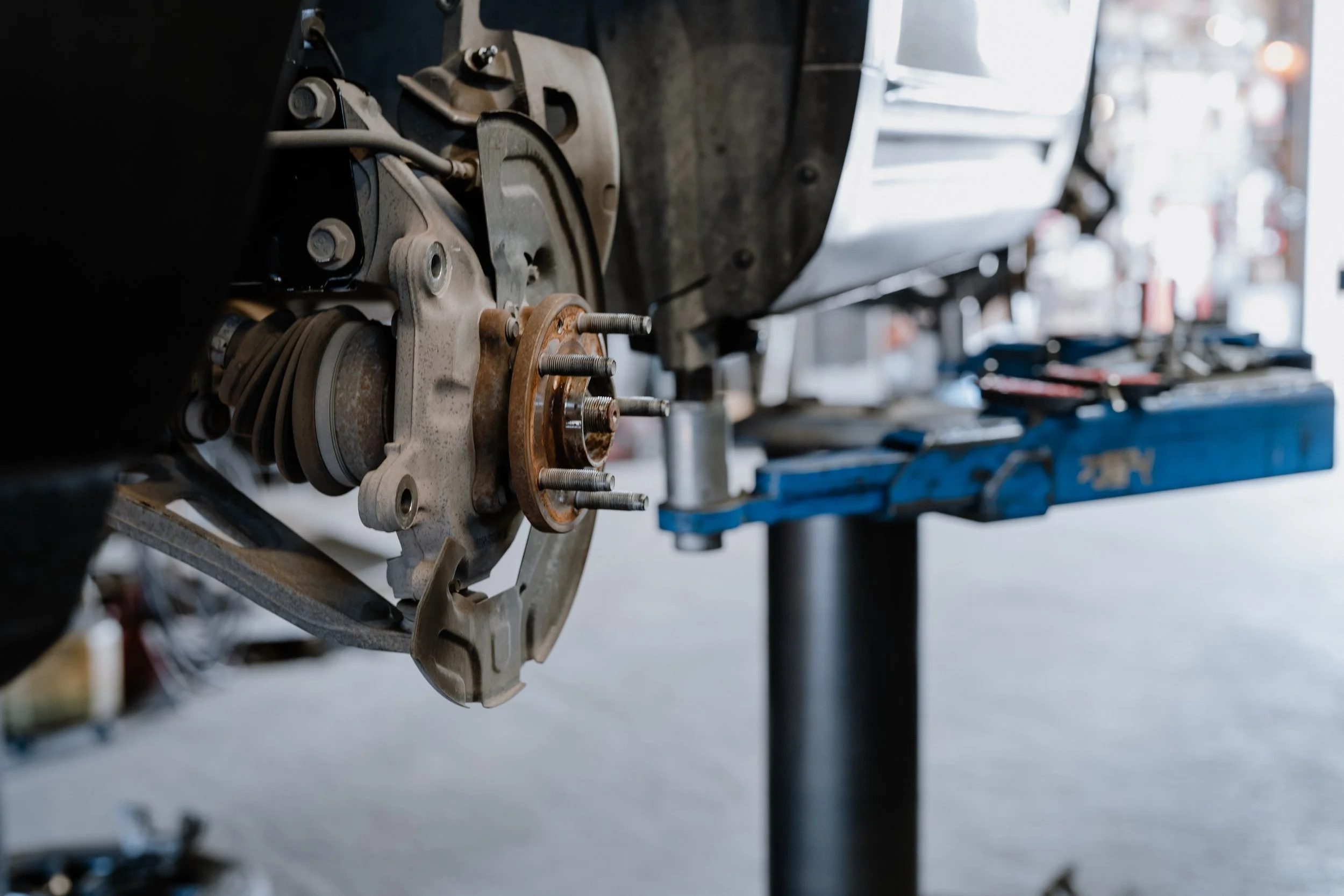 Close-up of a car's brake assembly and wheel hub, with the tire removed, in a garage or workshop setting.