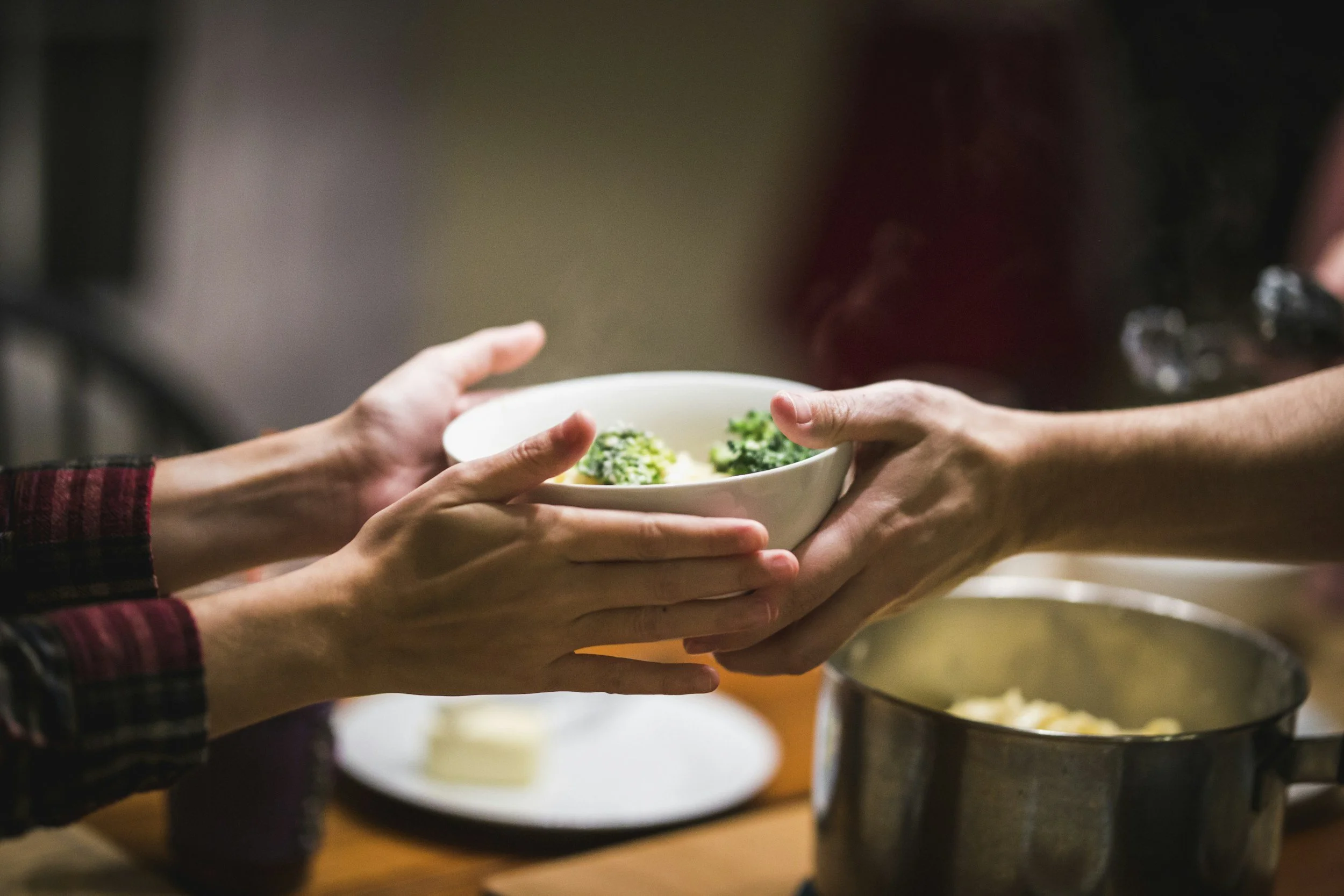 hands passing serving bowl across table to another set of hands