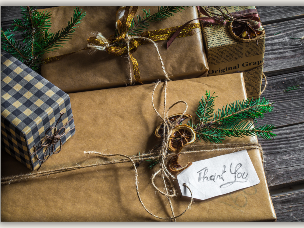 2 gifts wrapped in brown paper with twine bows and a handwritten thank you note. a dried orange and pine needles. another smaller wrapped gift with blue check paper
