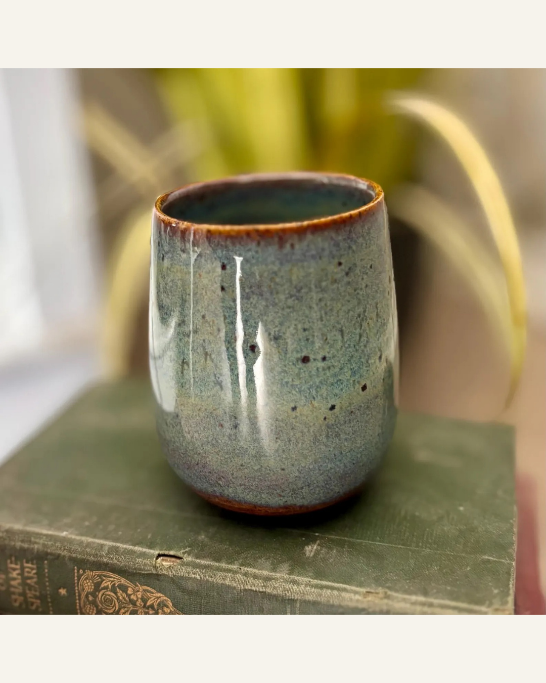 green handmade pottery wine glass or tumbler sitting on a green book