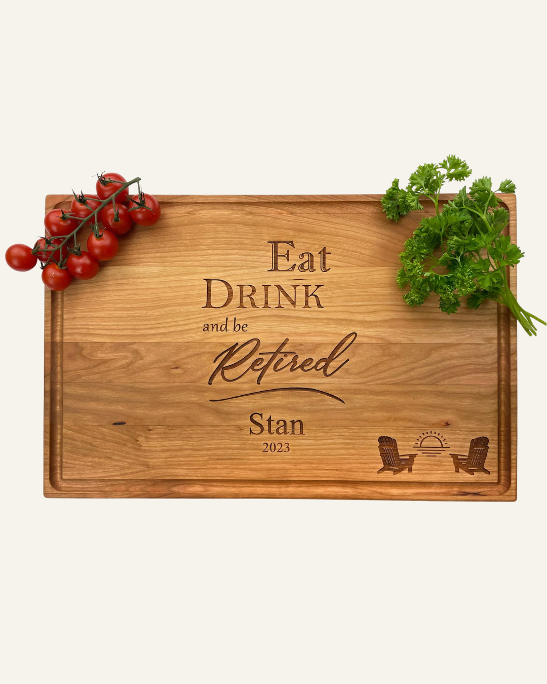 handmade wooden cutting board with text Eat Drink and be Retired Stan 2023 and image of 2 Adirondack chairs with sunrise. tomatoes and parsley in the corners