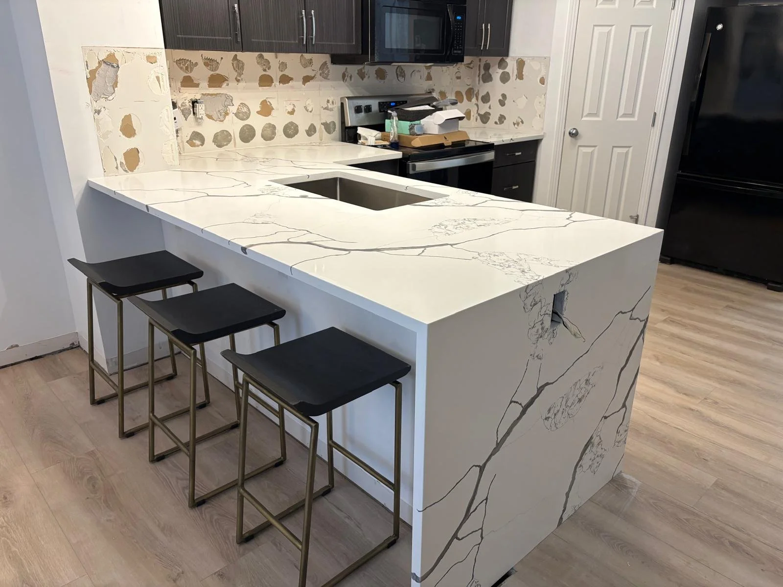 Kitchen island with white marble countertop featuring gray veining, with three black bar stools with gold frames