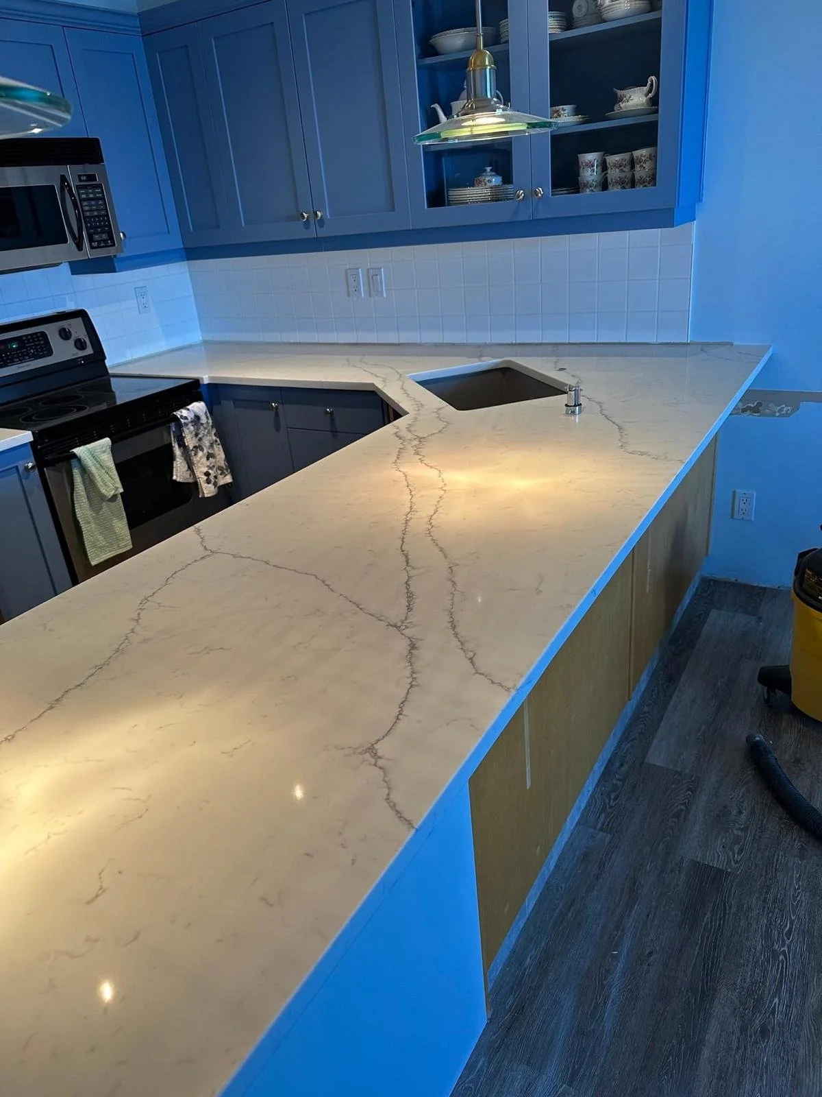 Kitchen with blue cabinets, a marble countertop with brown veining, a built-in sink, and a white tiled backsplash.