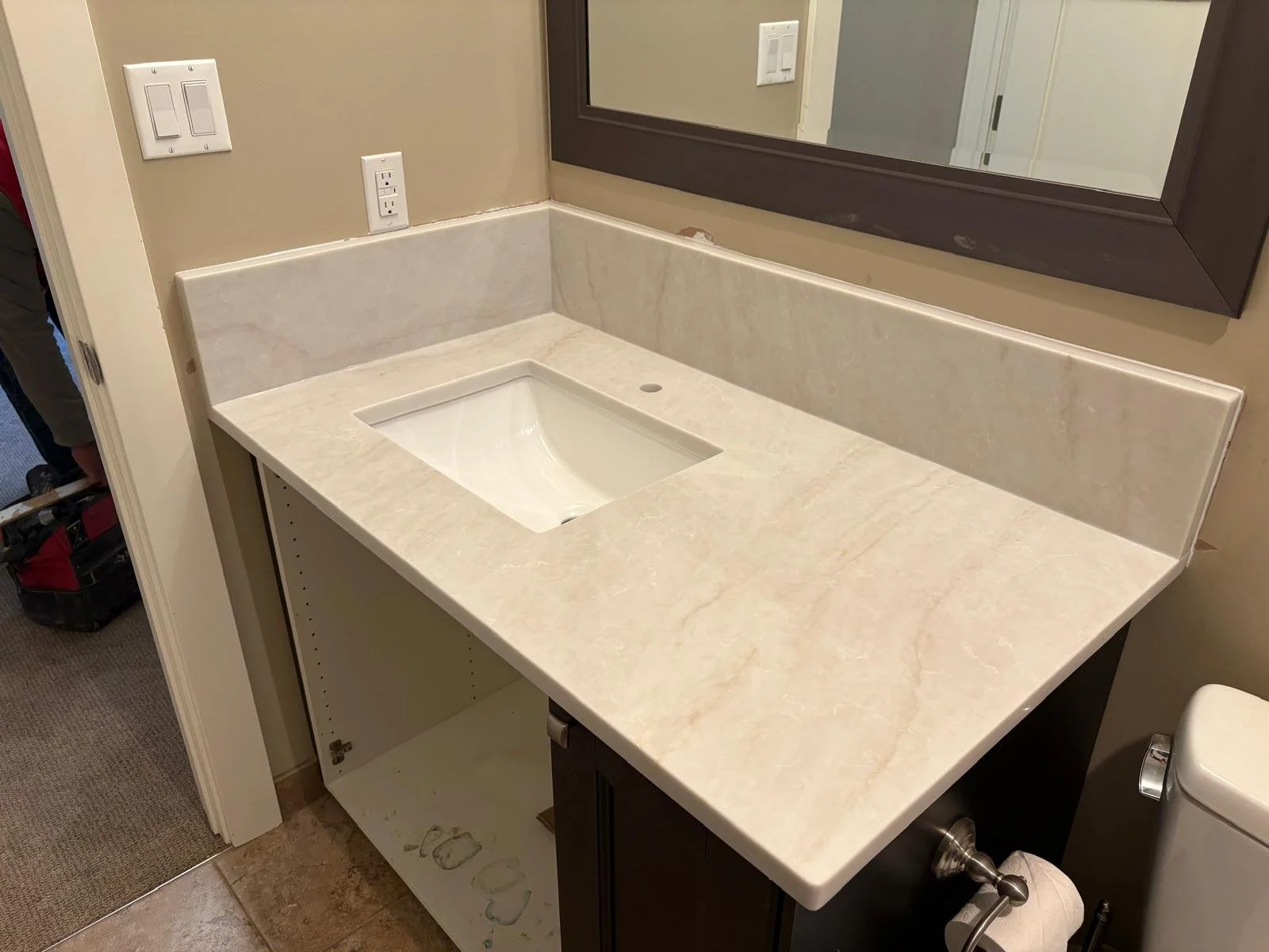 Bathroom vanity with a marble countertop and integrated sink, mirror above, and electrical outlets on beige wall.