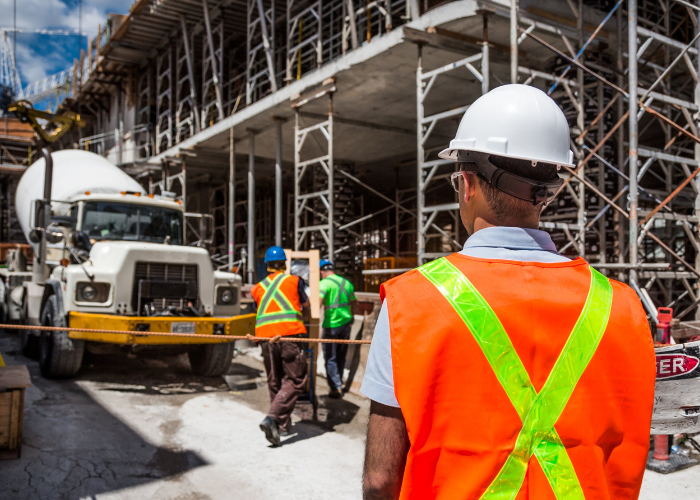 Construction workers on site with scaffolding, a cement mixer truck, and safety gear including helmets and vests.