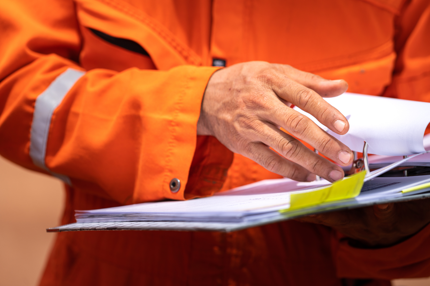Site safety in an orange jacket flipping through a stack of papers with yellow sticky notes.