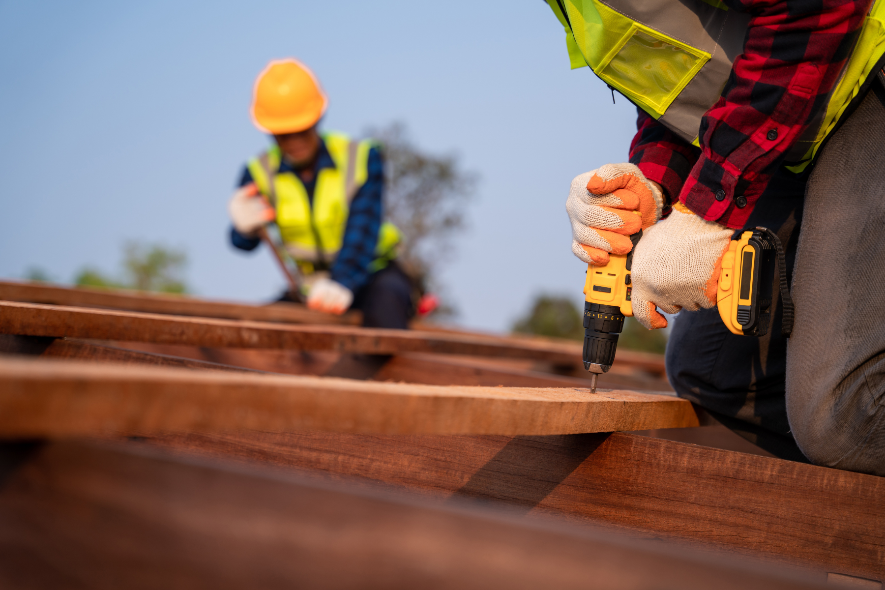 Construction workers wearing safety gear, including helmets and high visibility vests, working on a wooden structure outdoors.