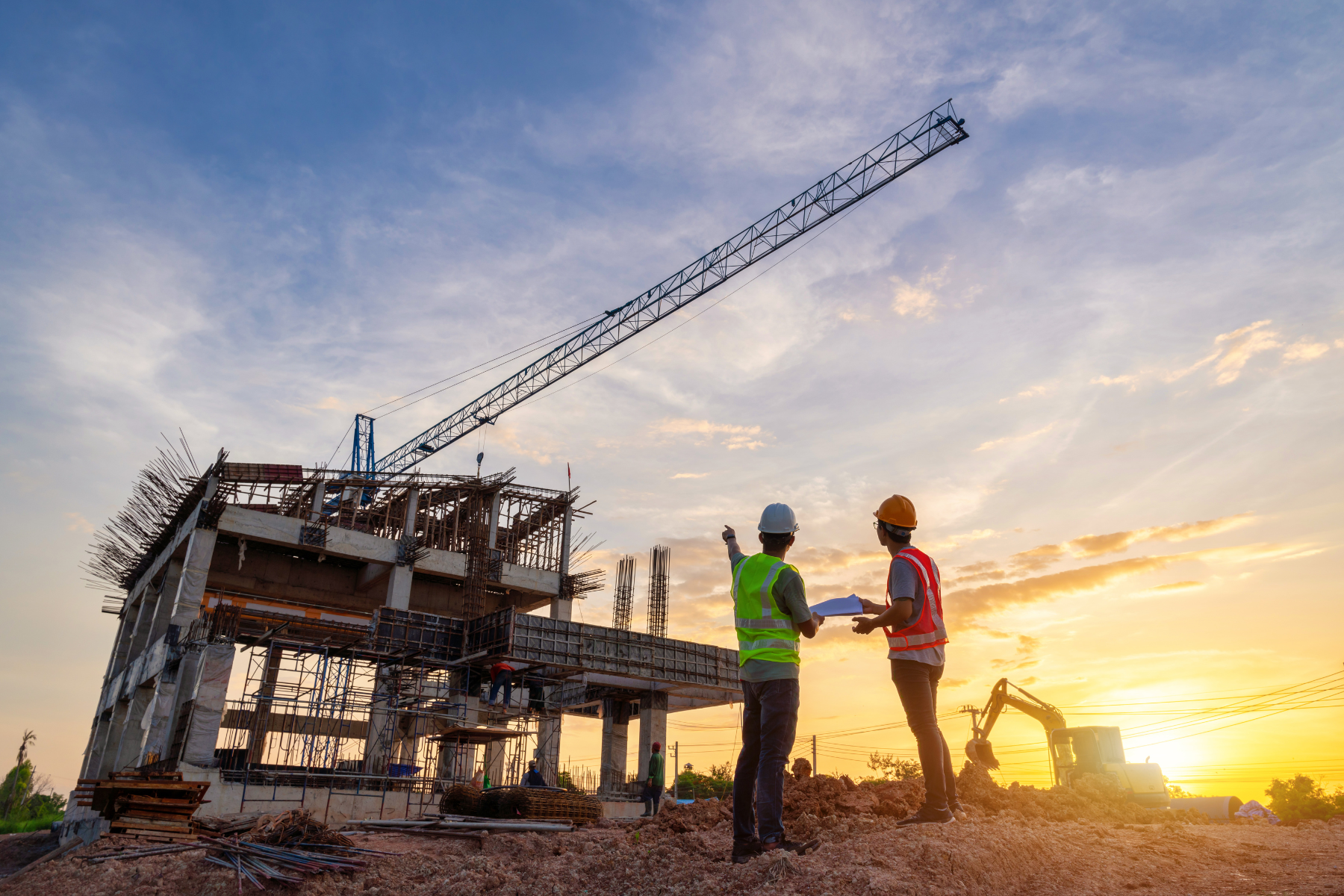 Construction workers in safety gear discussing building progress at sunset, with crane and construction site in the background.