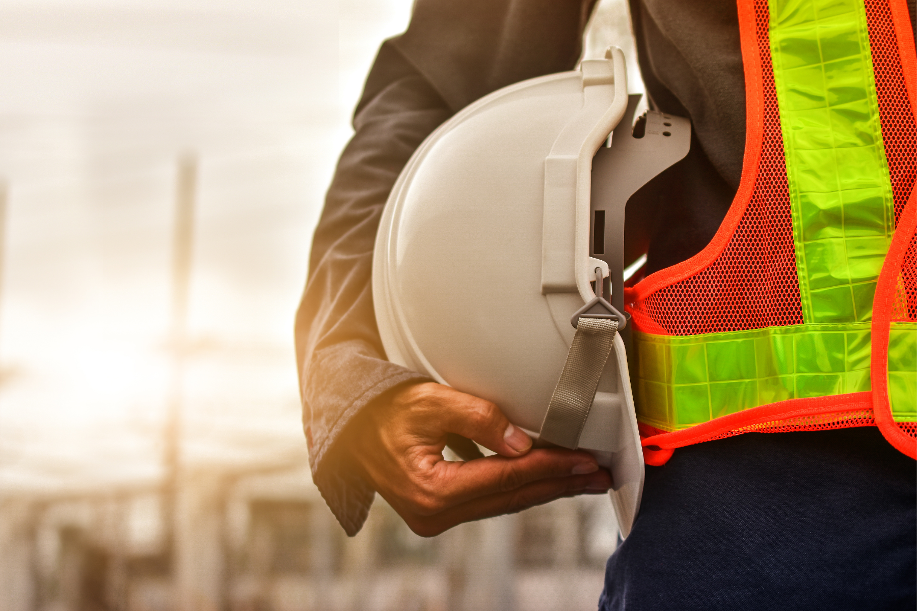 Construction worker wearing a neon safety vest holding a white hard hat.