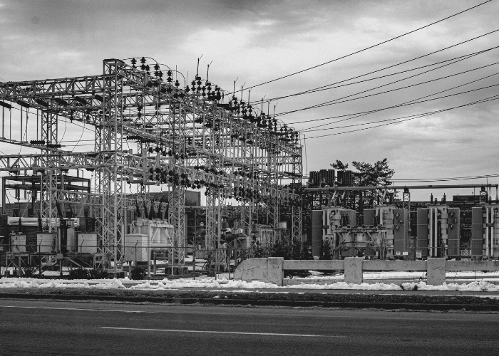 Power substation with electrical transformers and wiring along a road in black and white.