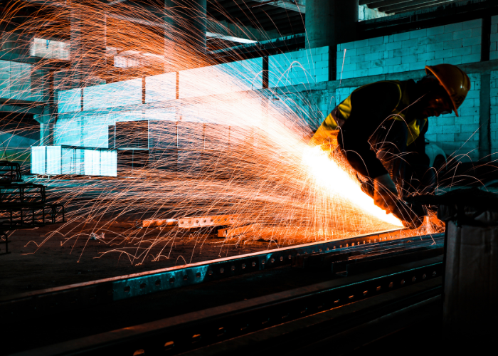 A worker in safety gear welding metal, with sparks flying in a factory or industrial setting.