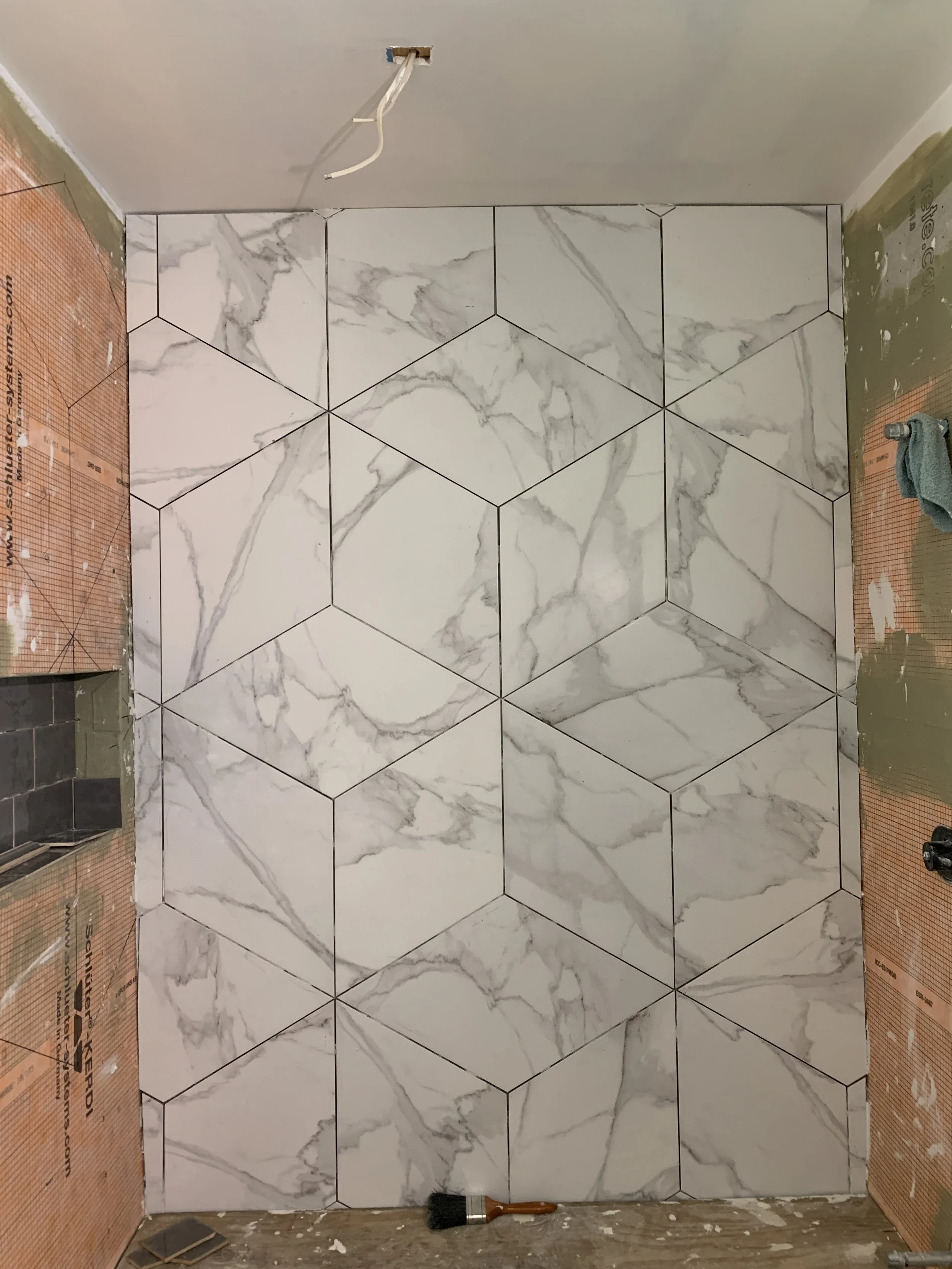 Cypress Works Massachusetts, a modern walk-in shower with clear glass door, white tiled walls, and a gray mosaic tile floor, in a bathroom with large beige floor tiles and a gray bath mat.