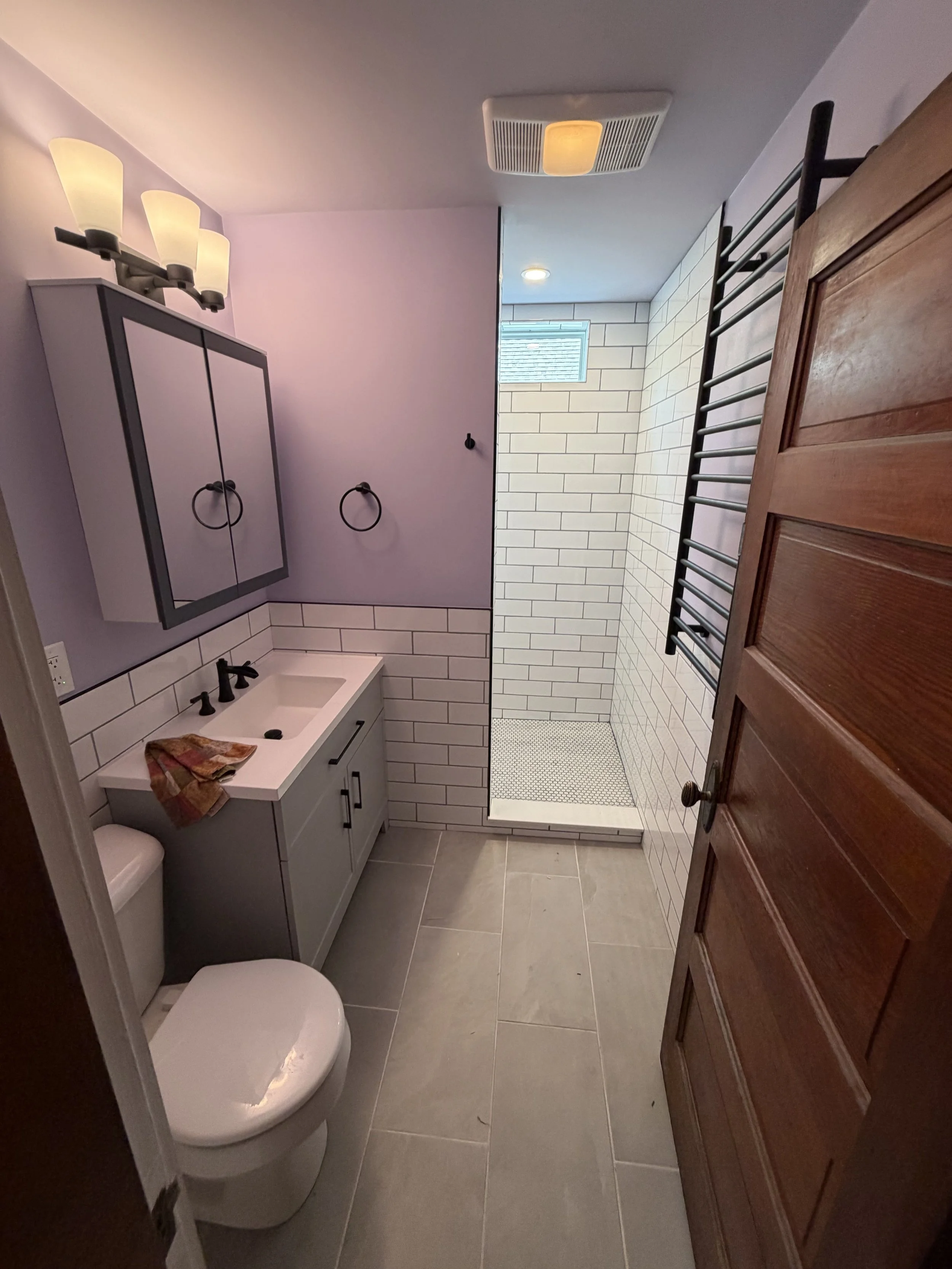 Cypress Works Massachusetts, bathroom remodel in fitchburg featuring a vanity with a sink, a toilet, a wall-mounted medicine cabinet with mirror, towel rings, a walk-in shower with white subway tiles, a small window, and a heated towel rack. 