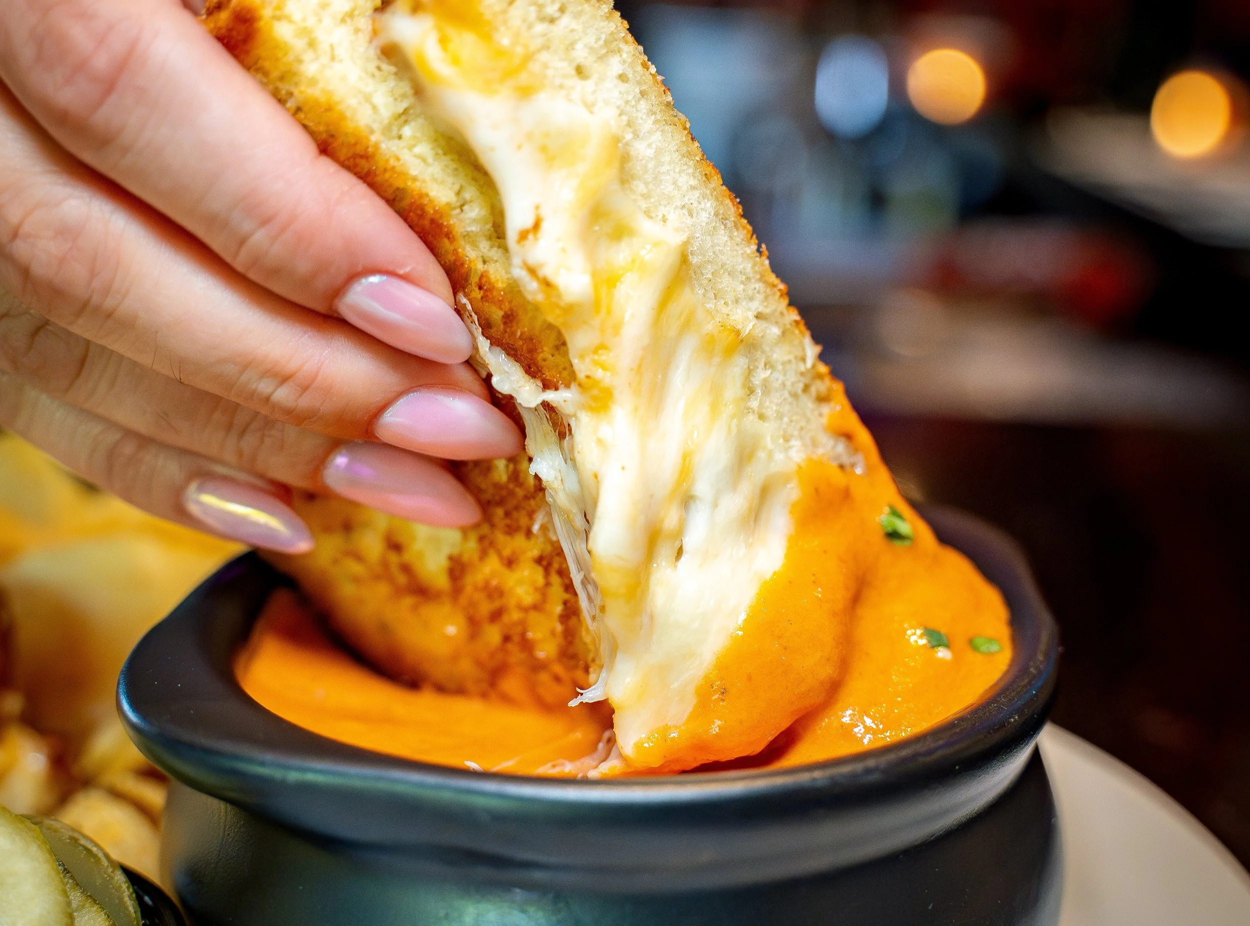 Close-up of a grilled cheese sandwich with melted cheese being dipped in tomato soup