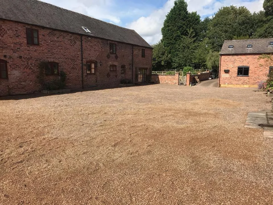 A large gravel courtyard outside of red brick buildings, with trees and a partly cloudy sky in the background.