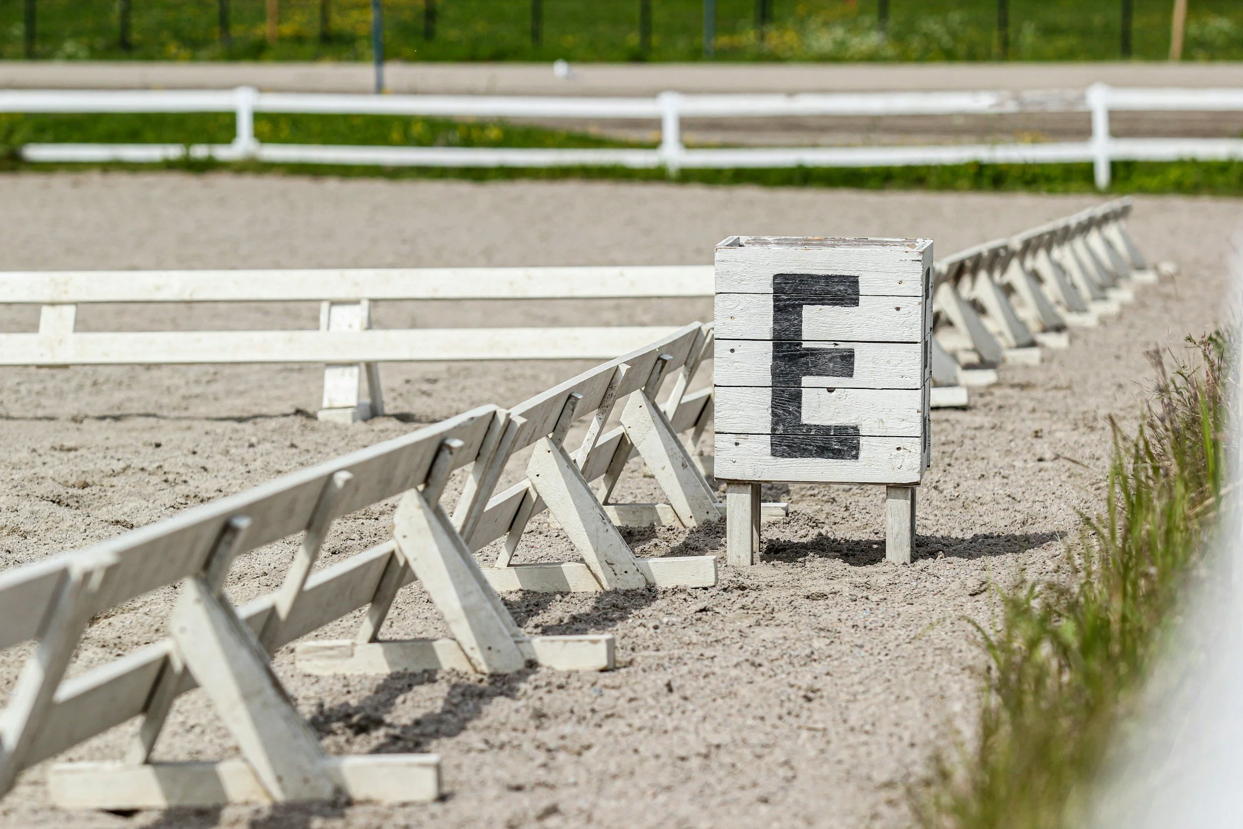 Empty horse riding arena with white fences and a wooden marker marked with the letter E.