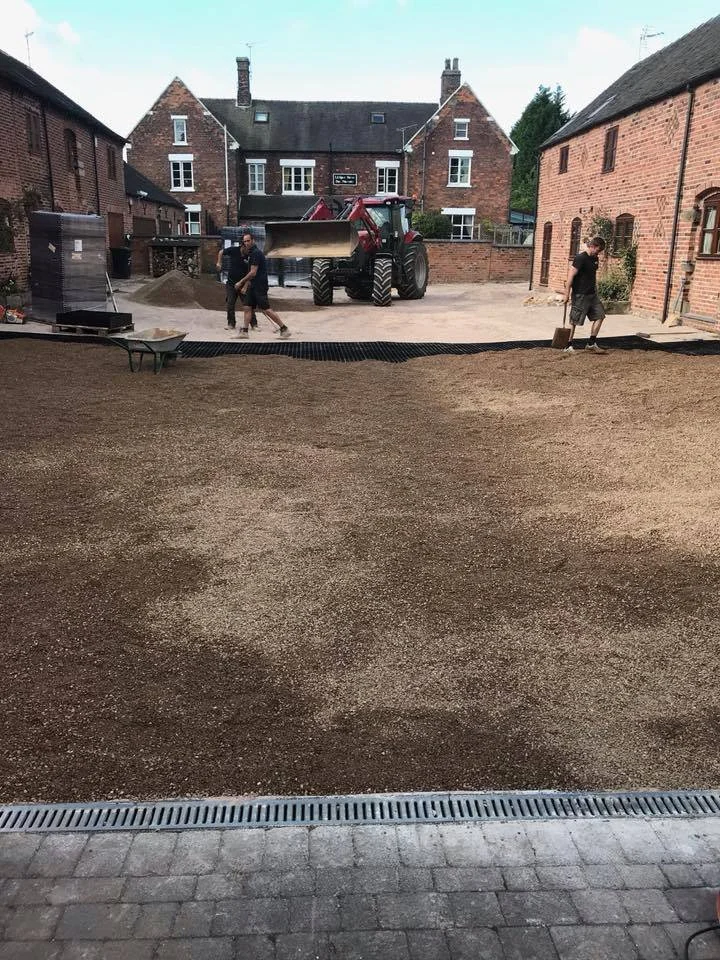 People working on landscaping with a tractor and shovels in a backyard between brick houses.