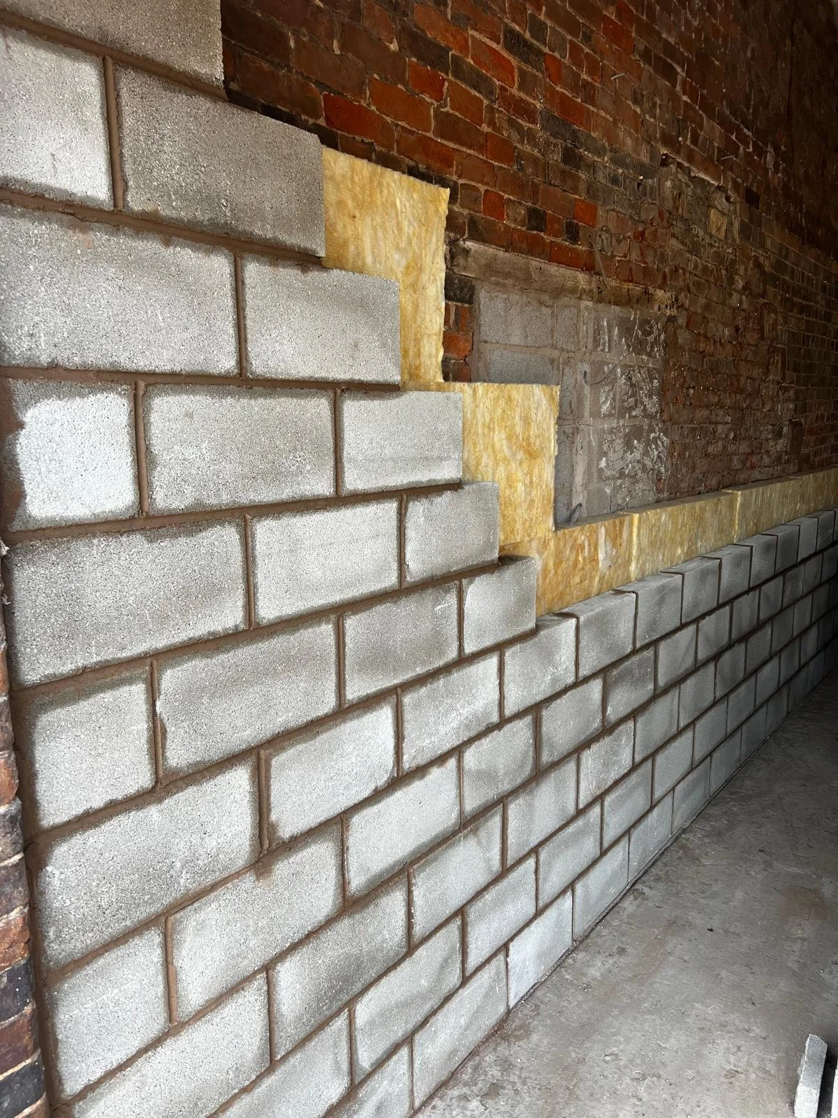 Interior wall under construction showing layers of brick, insulation, and concrete blocks.