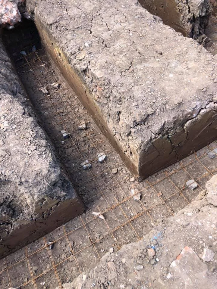 Close-up of a construction site showing a concrete foundation with rebar, dirt, and debris.