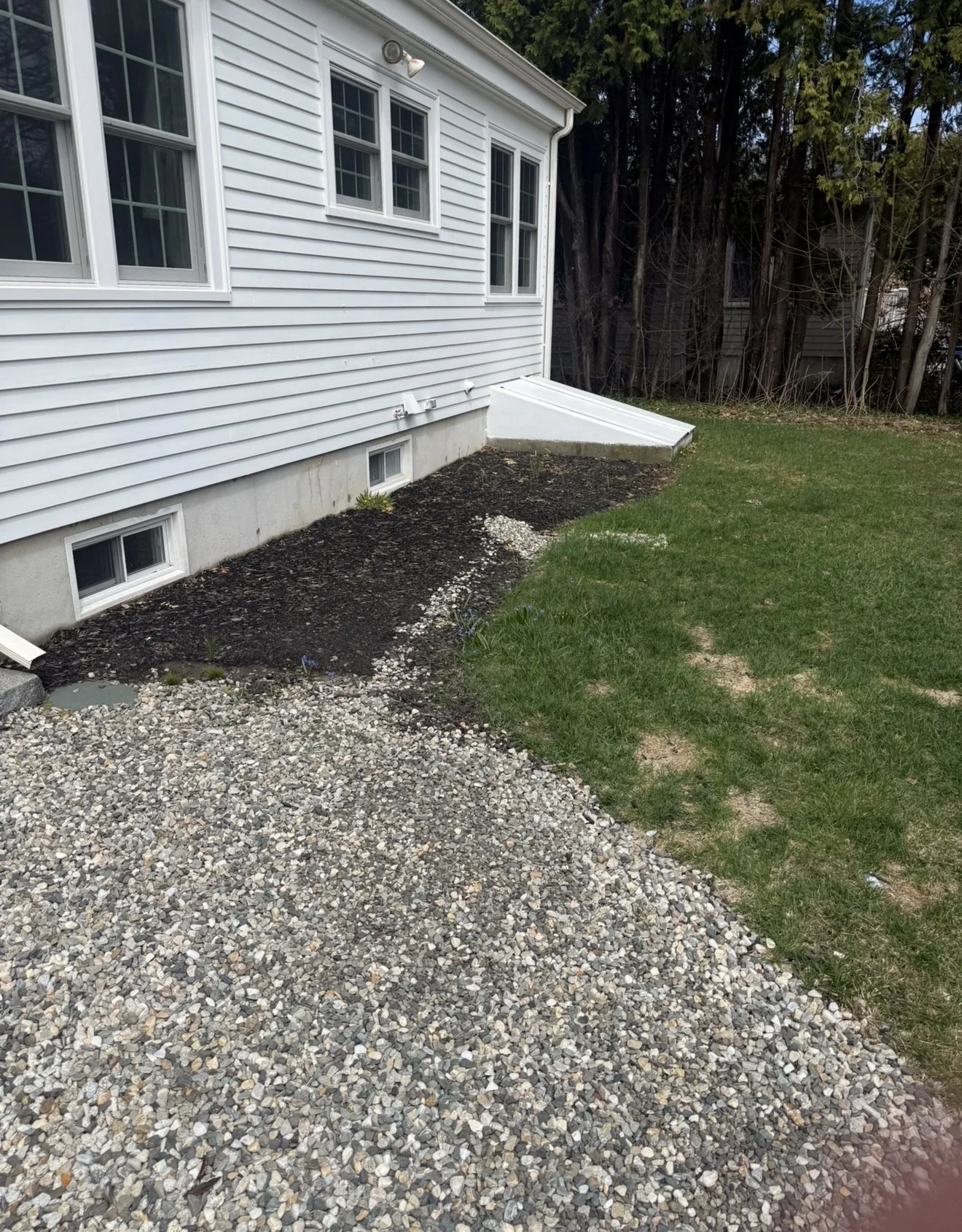 Backyard with a house, new gravel pathway, lush green grass, small garden bed, and wooded backyard.
