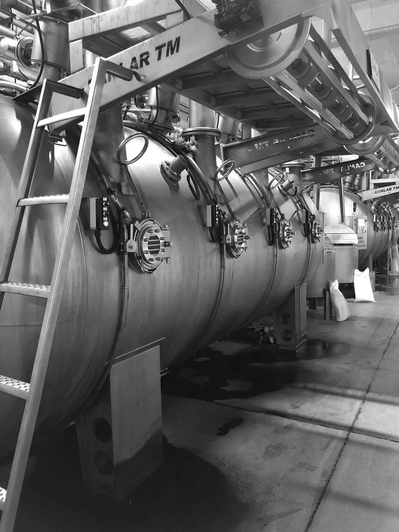 Large industrial stainless steel pressure vessel with multiple valves, pipes, and a ladder in an industrial facility.