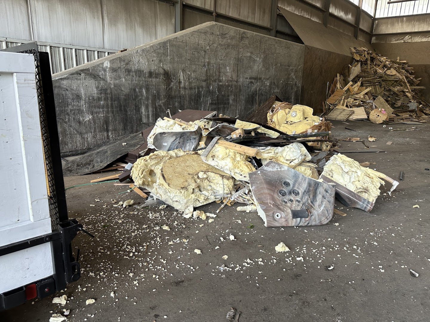 Pile of construction or insulation material and debris scattered on the floor inside a warehouse or industrial building, with a dark wall and wooden scraps in the background.