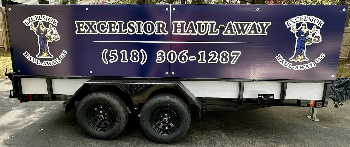 A purple trailer with the branding and contact information for Excelsior Haul-Away LLC, featuring the logo of Lady Justice holding scales and a sword.