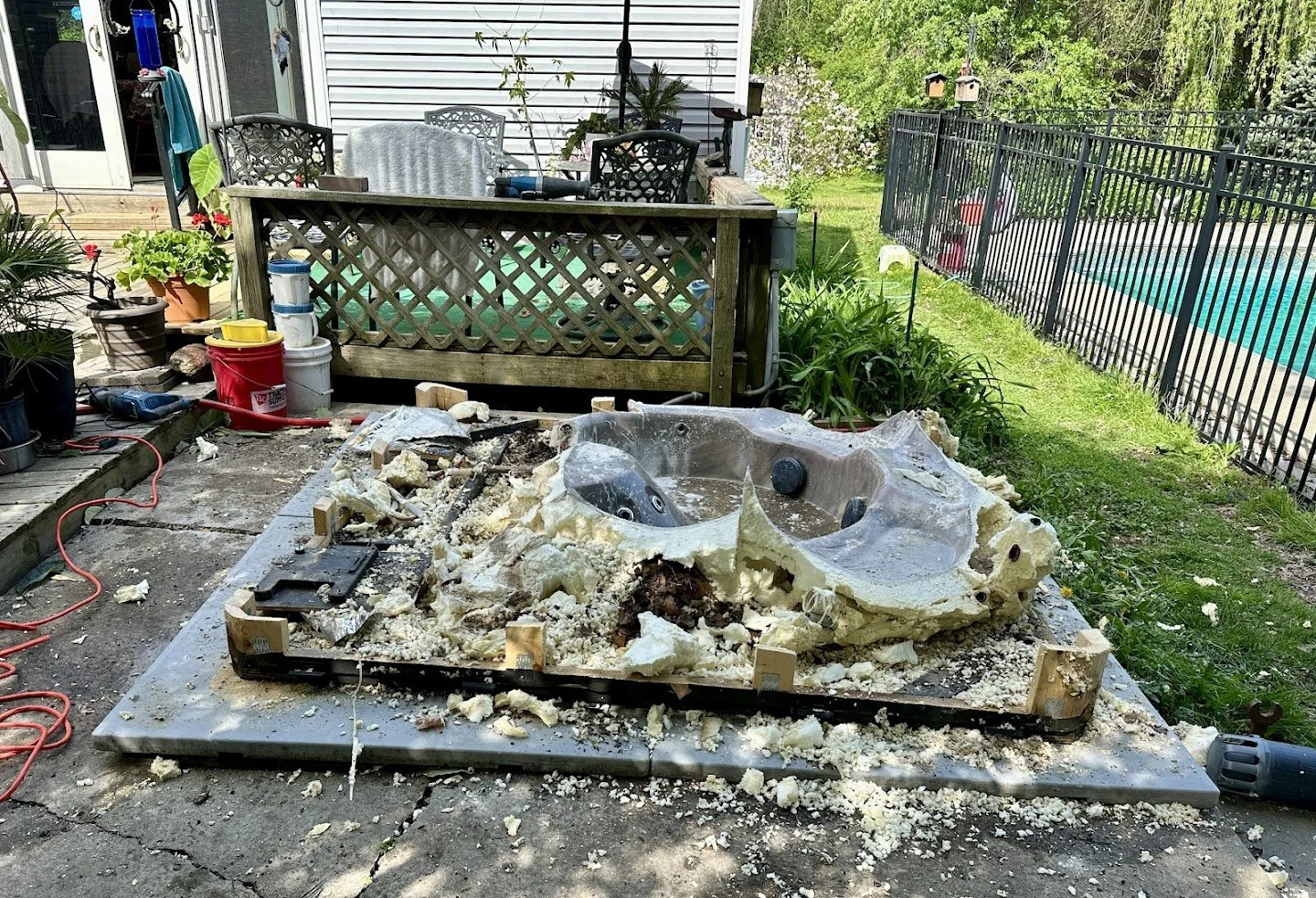 Yard with hot tub renovation in progress, insulation materials scattered, tools, and work debris near patio, backyard with swimming pool, fences, and garden plants.