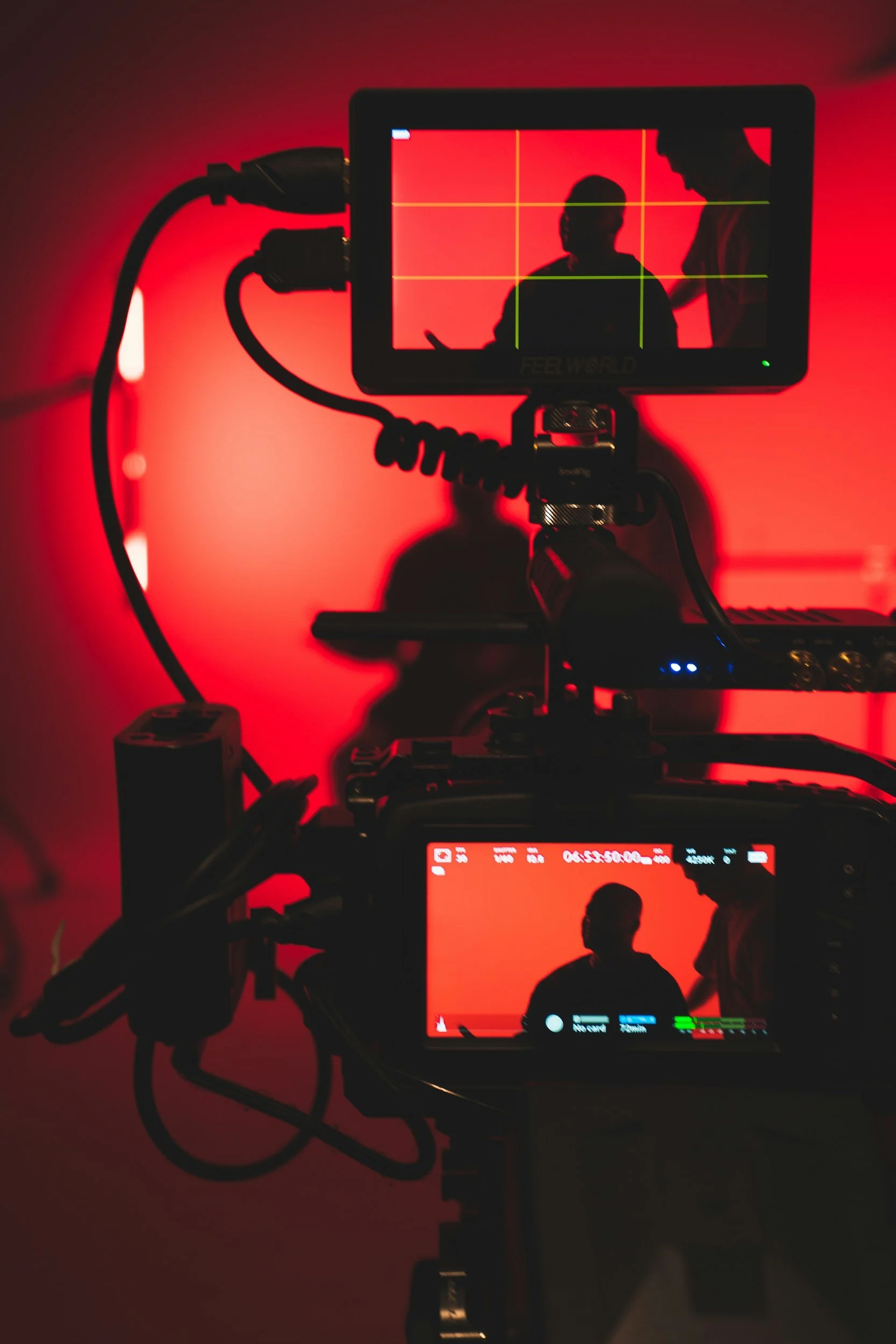 A camera monitor shows a silhouetted person in front of a red background being filmed by a camera.
