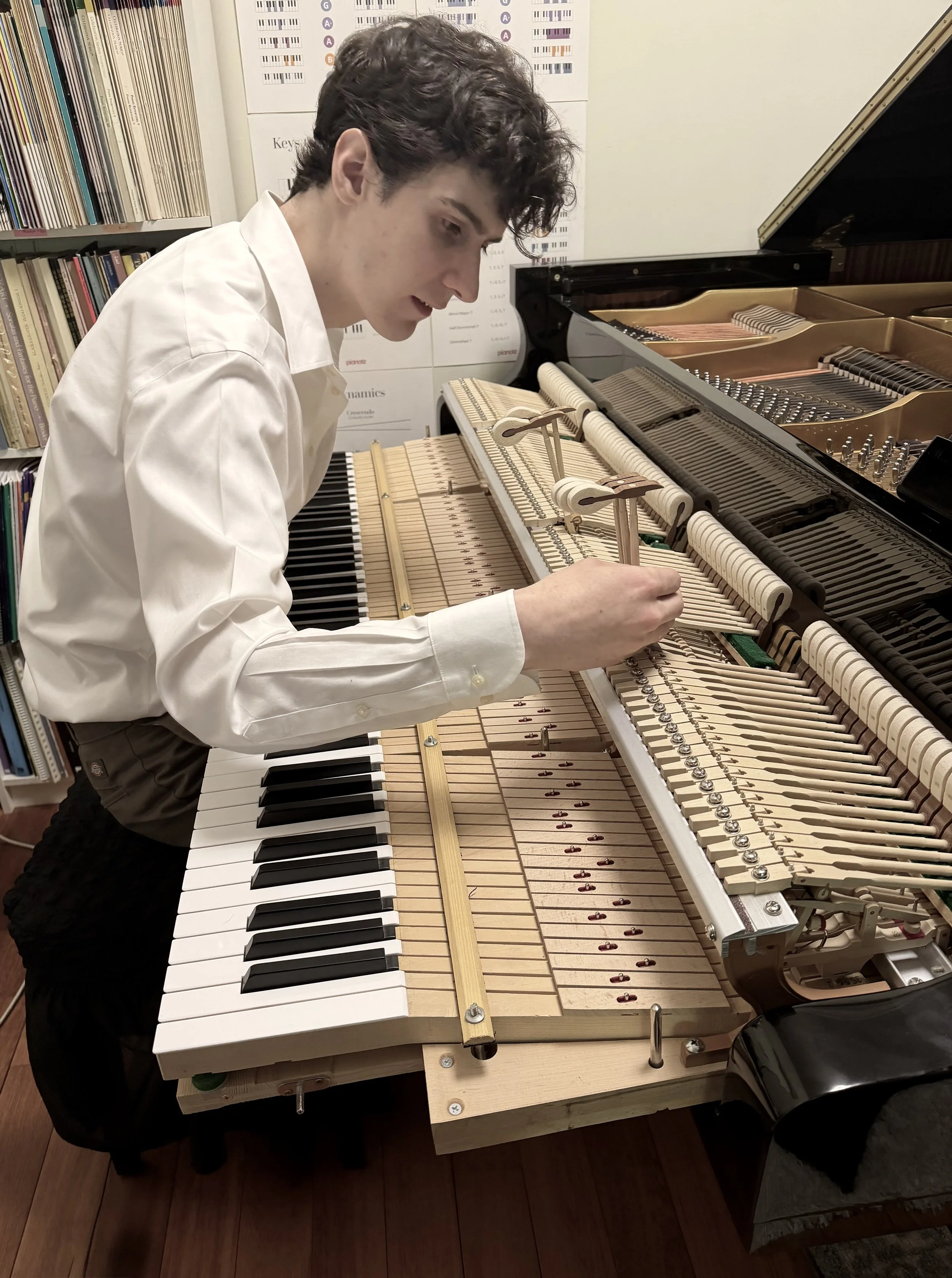 Caleb of Caleb's piano care and repair is working on the inside of a piano. The piano lid is open, revealing the strings and hammers. He is inspecting the piano for possible repairs