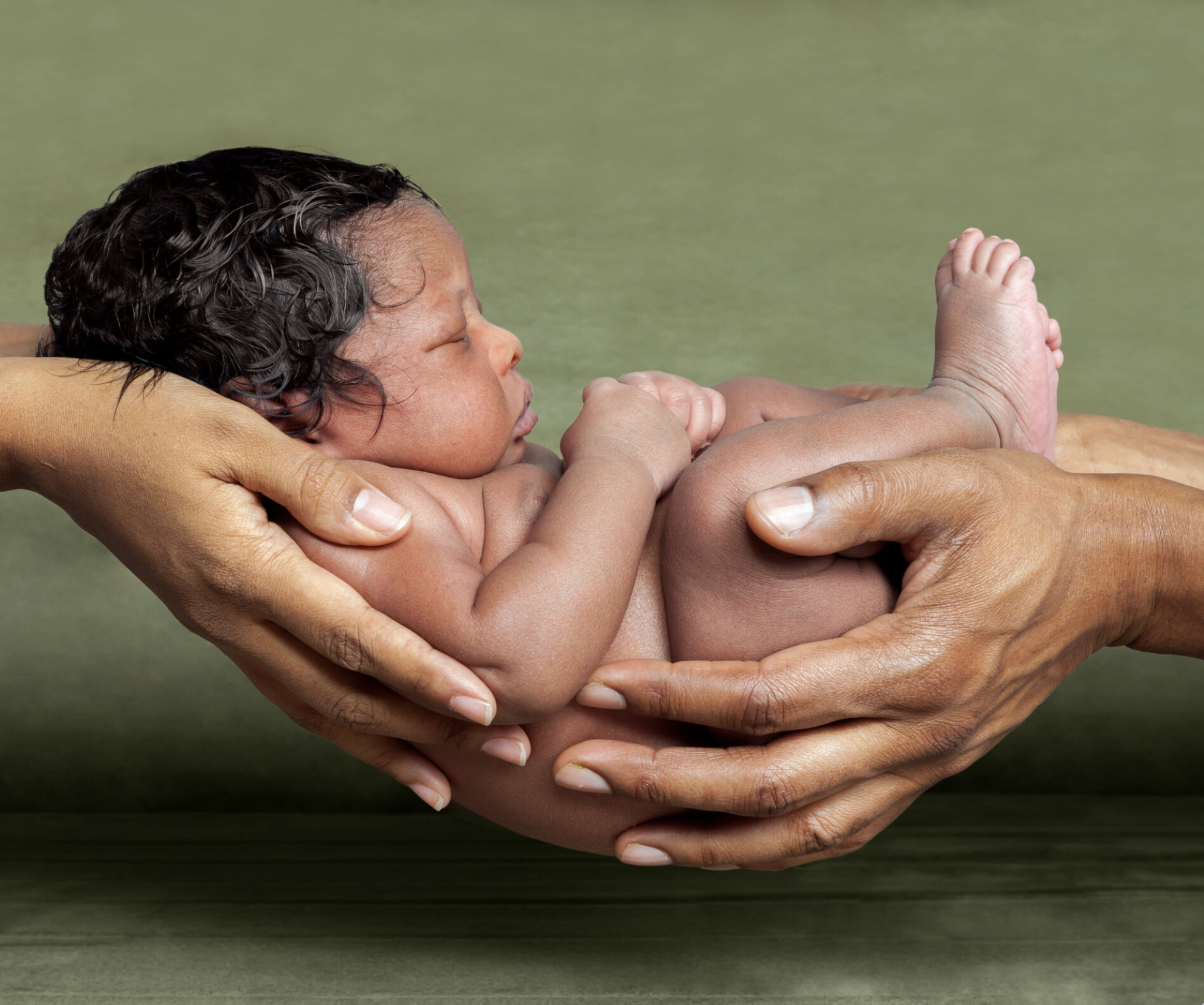 A newborn baby sleeping peacefully in someone’s hands, with a green backdrop.