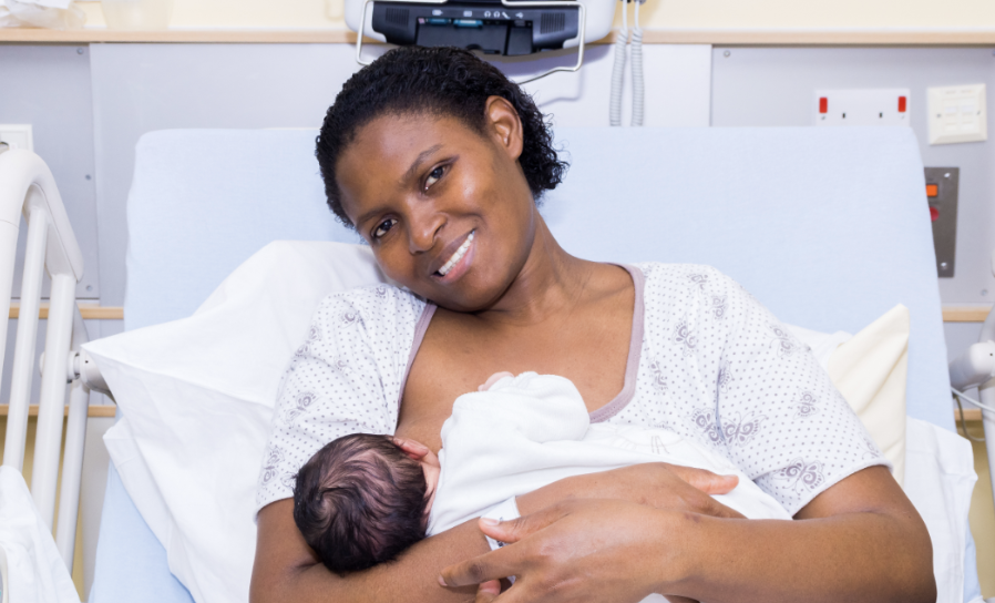 A woman in a hospital bed holding a newborn baby, smiling in a hospital room.