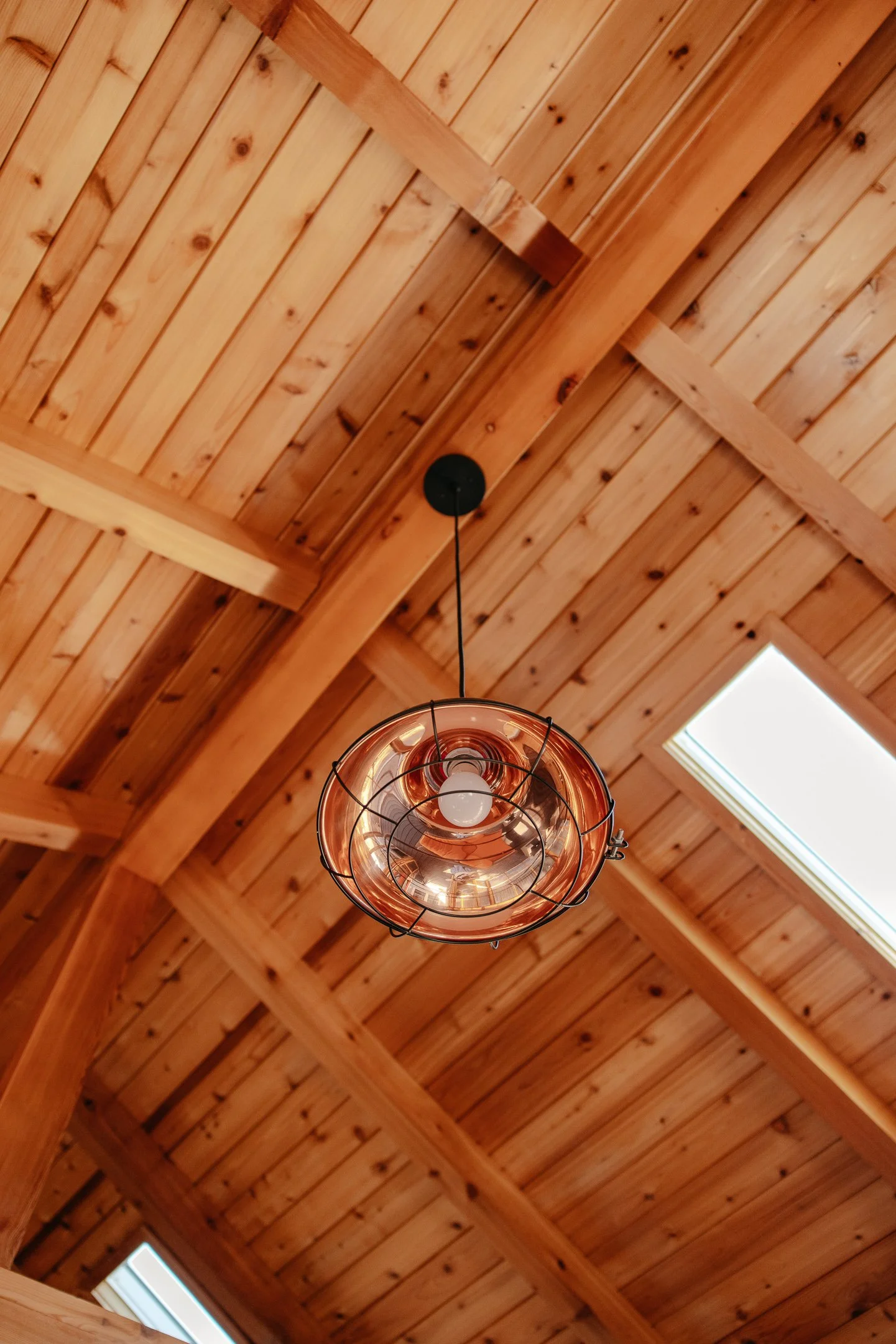 A wooden ceiling with beams and planks, a hanging copper-colored light fixture, and a rectangular skylight.