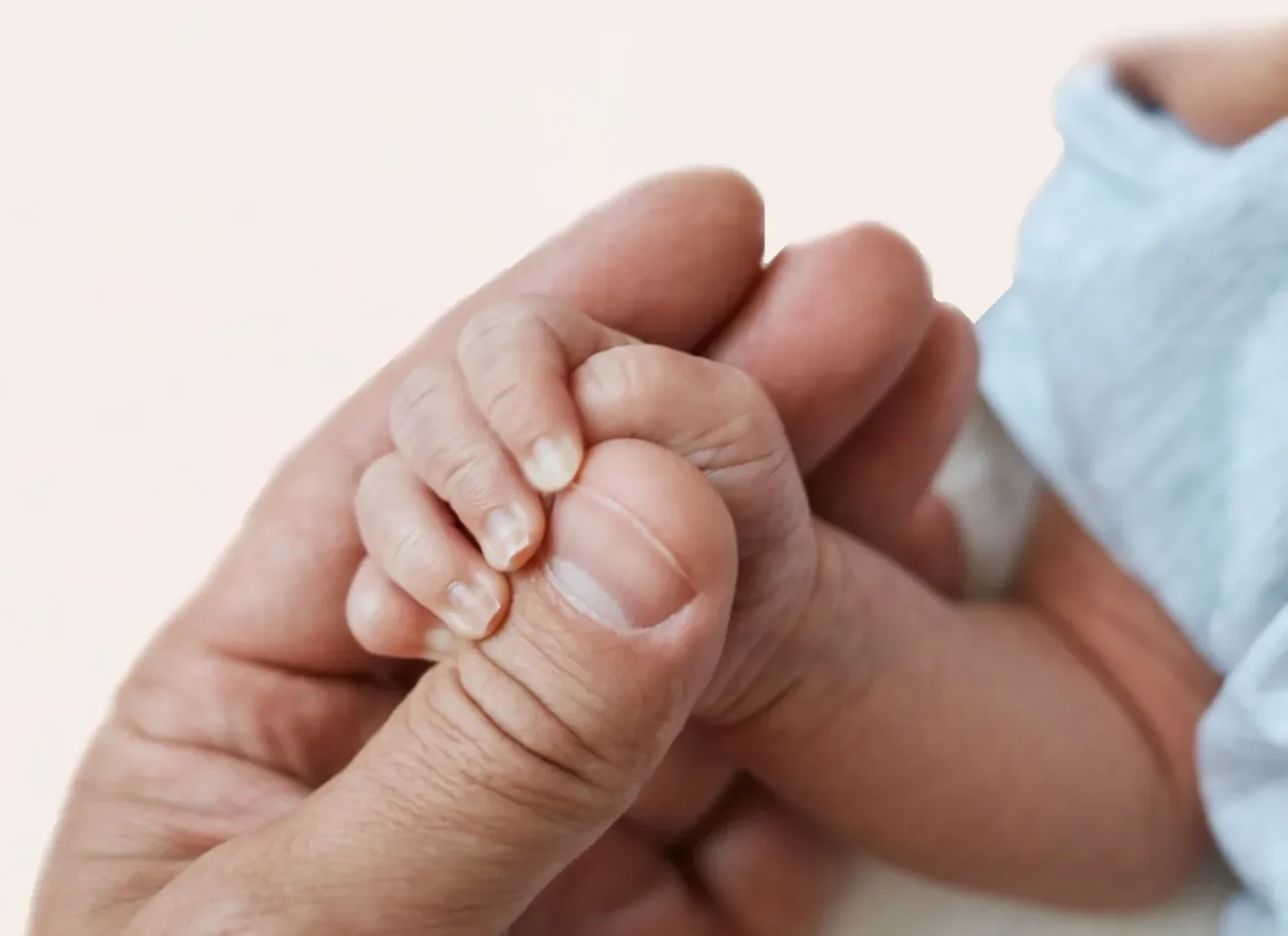 Close-up of an adult holding a baby's hand, representing early childhood care, genetic testing, and support for families.