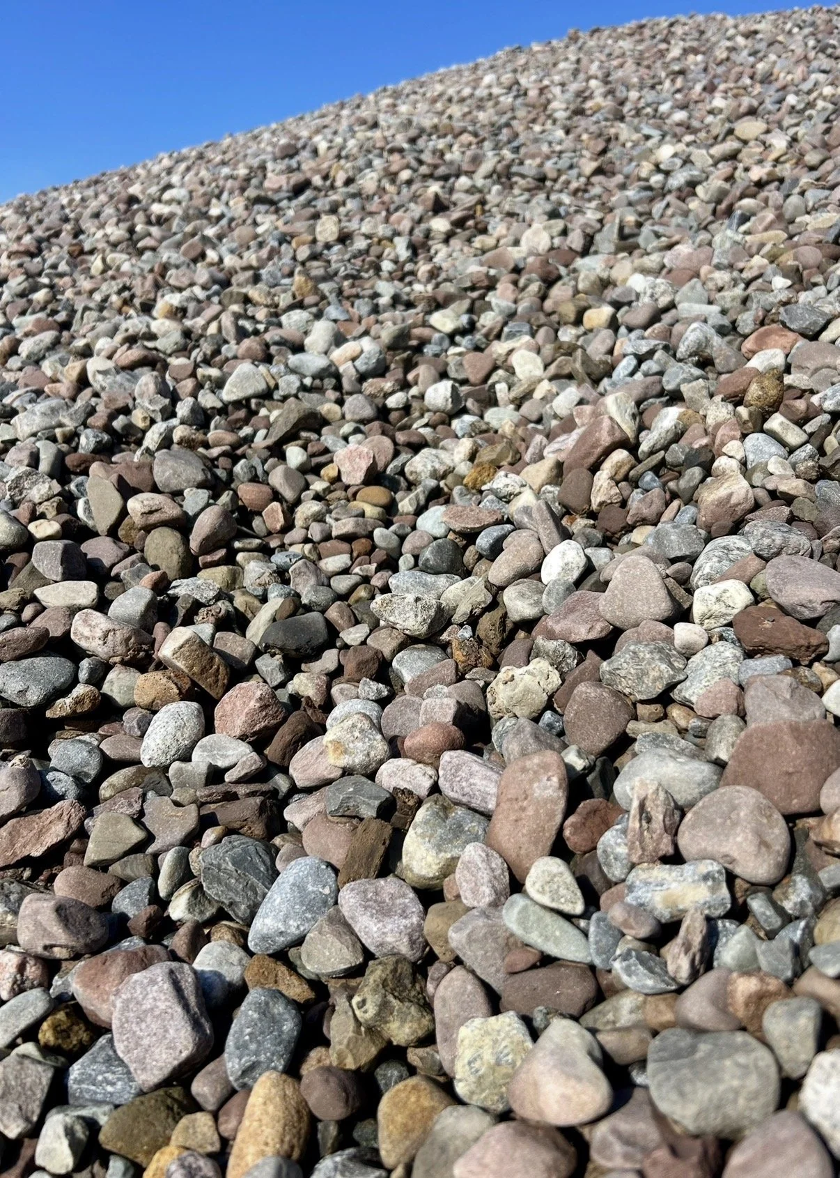 Close-up view of a large pile of small, multicolored rocks under a clear blue sky.