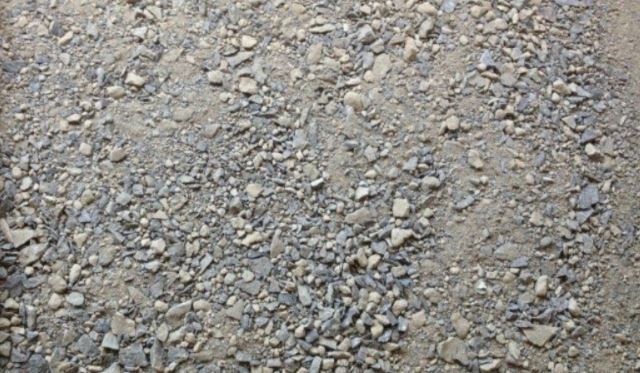A ground surface covered with small gray and white rocks, with a coin and a small green object among the rocks.
