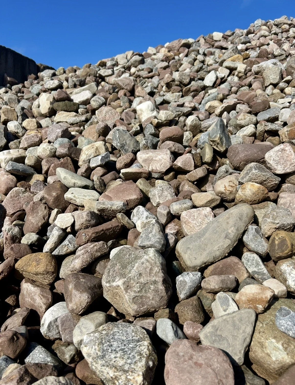 Close-up of various colored small rocks and gravel on a sloped surface under a clear blue sky.