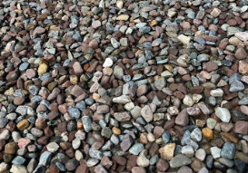 Close-up view of a gravel surface made up of small, multicolored rocks and pebbles with a few tiny green plants growing between them.