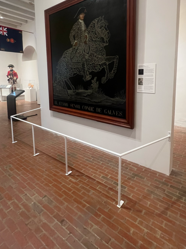 A framed artwork depicting a historically dressed man on horseback, titled 'El Foso Señor Conde de Gales,' displayed in a museum setting.