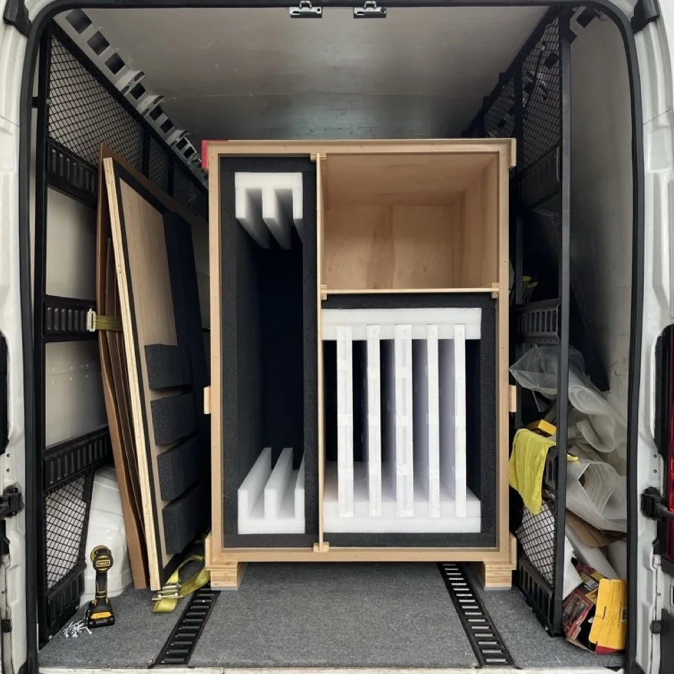 Inside a vehicle, there is a wooden crate with precise foam padding, and tools. Showing off the detailed work of packing art.
