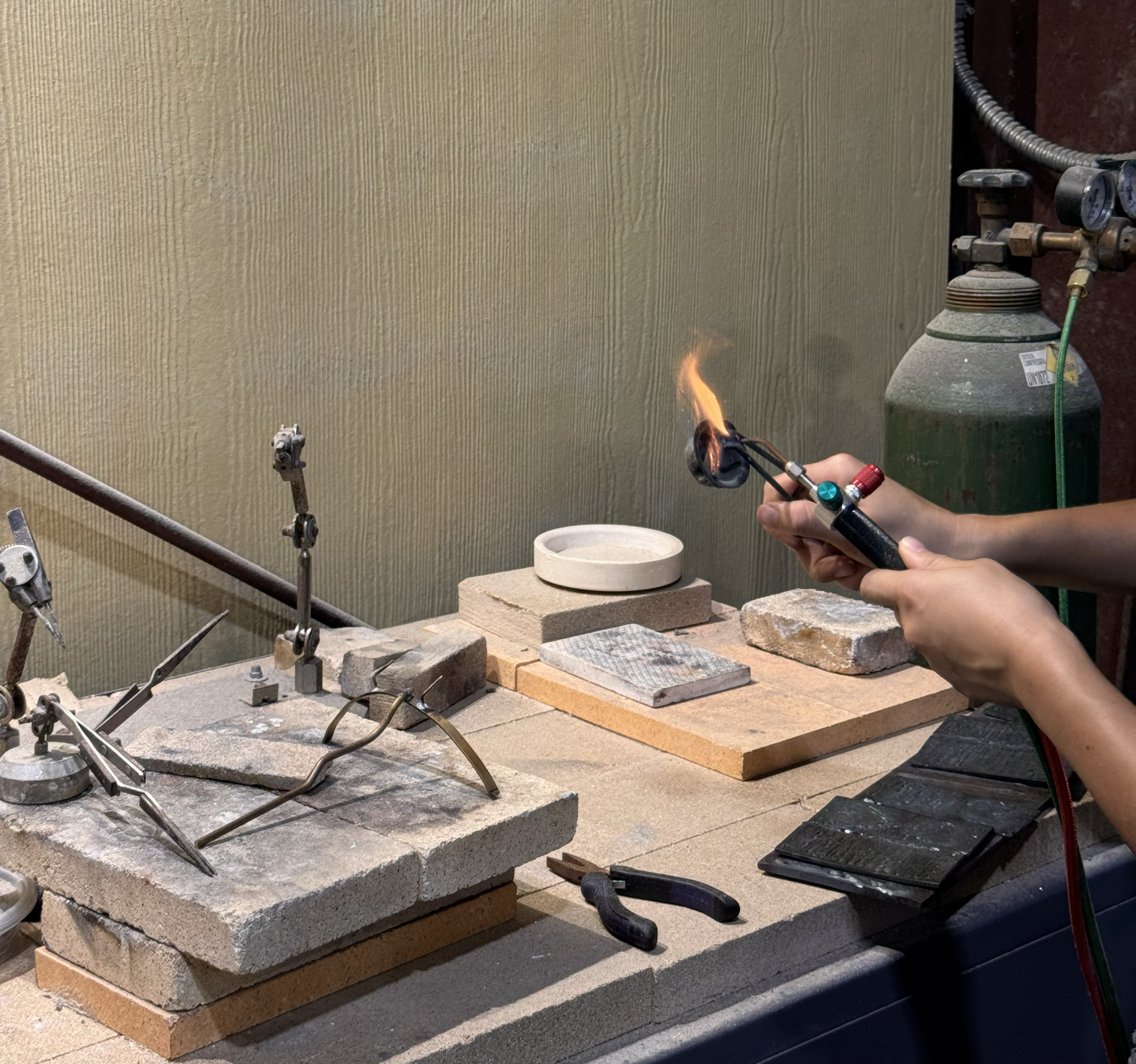 A person working with a blowtorch on a stone surface, with various tools and stones on a workbench in a workshop.
