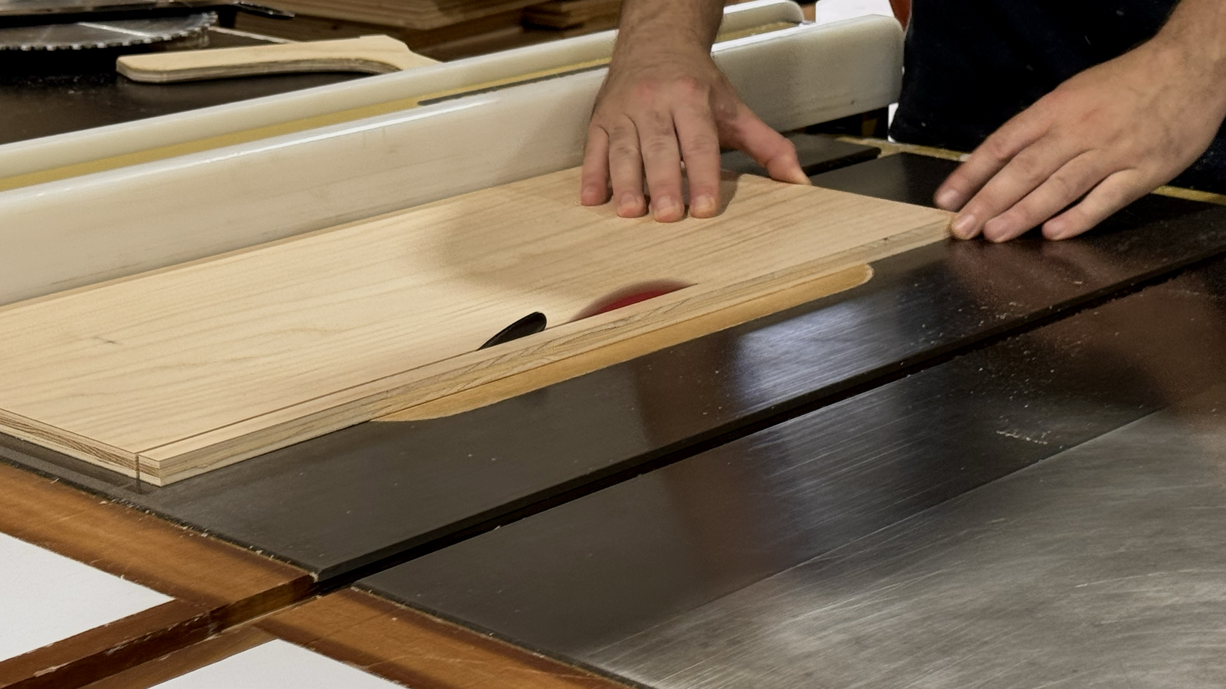 Close-up of a person's hands guiding a piece of wood through a table saw.