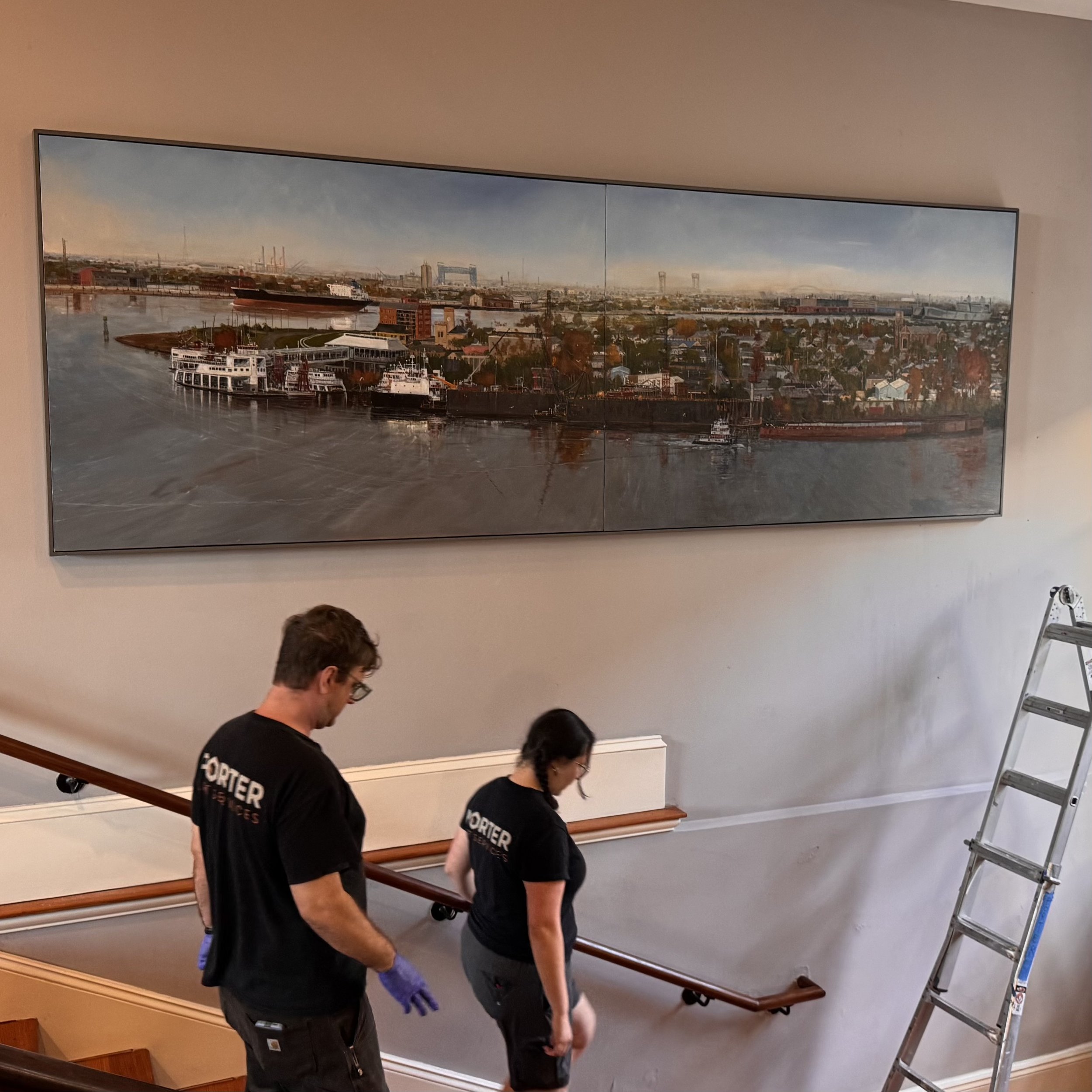 People descending a staircase in an indoor setting with a large artwork of a cityscape hanging on the wall.