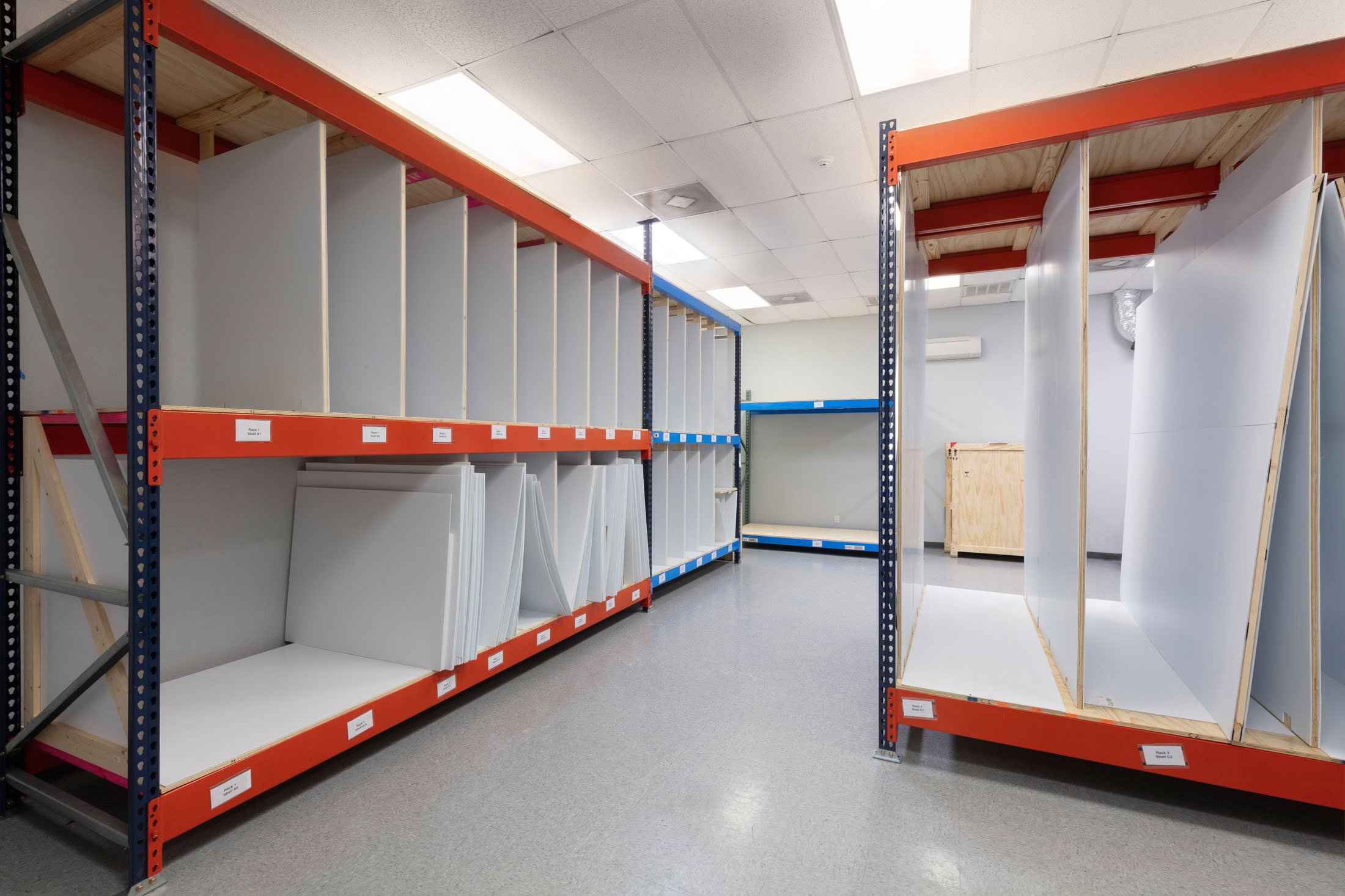 Empty storage shelves with white boards and labels in an industrial or warehouse setting.