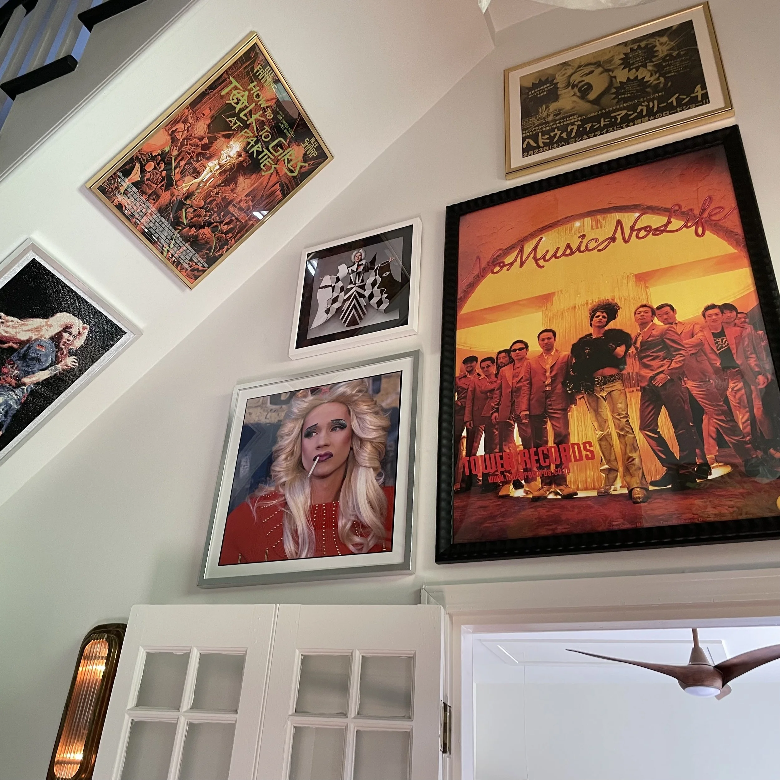 Various framed posters arranged on a white wall, including artwork from Tower Records, a woman with blonde hair and makeup, and a vintage Japanese poster.