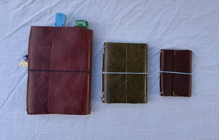 Three leather journals or notebooks of different sizes placed on a white surface.