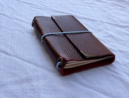 Red leather-bound journal with elastic band on a white fabric surface.