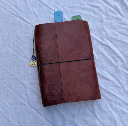 A purple leather notebook with a black elastic band and a small decorative key charm attached to the elastic band, resting on a white surface.