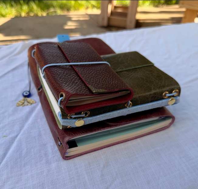 Stack of multiple leather journals on a white cloth surface outside.